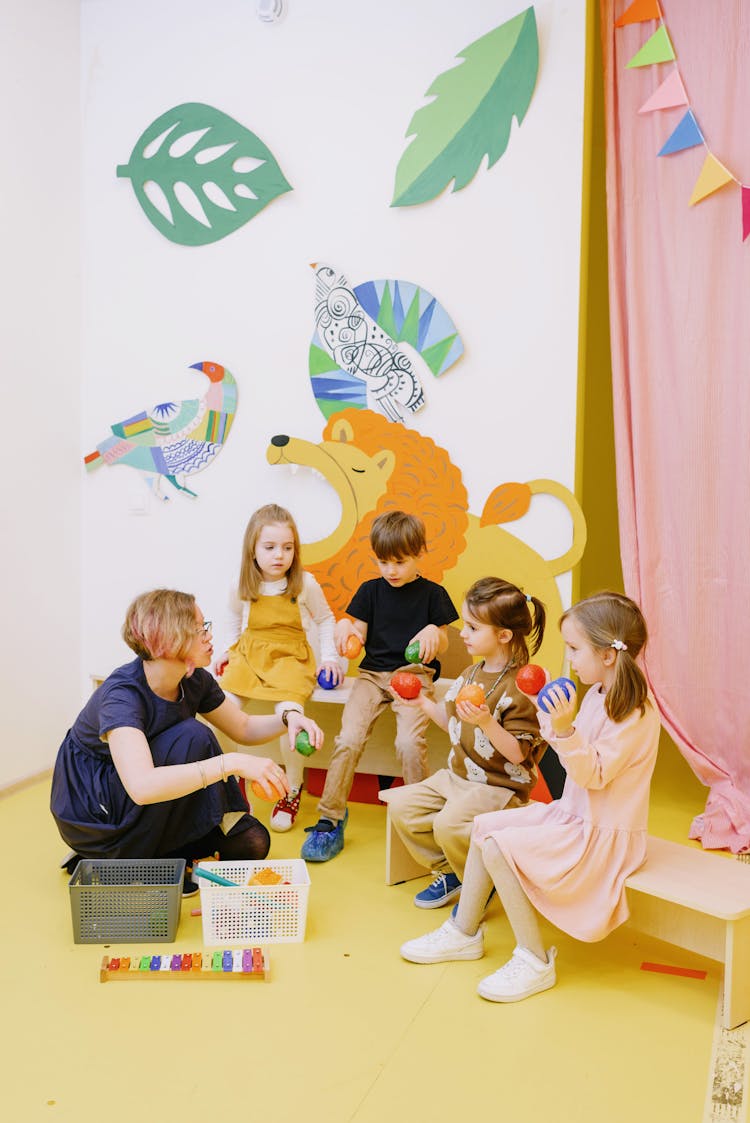 Kids Holding Colorful Balls While Listening To Their Teacher