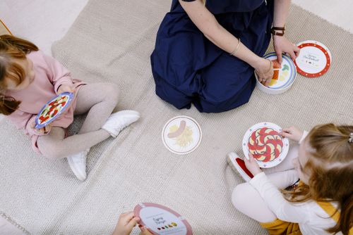 Free Three children and a teacher playing a card game on a blanket. Engaged and educational fun. Stock Photo
