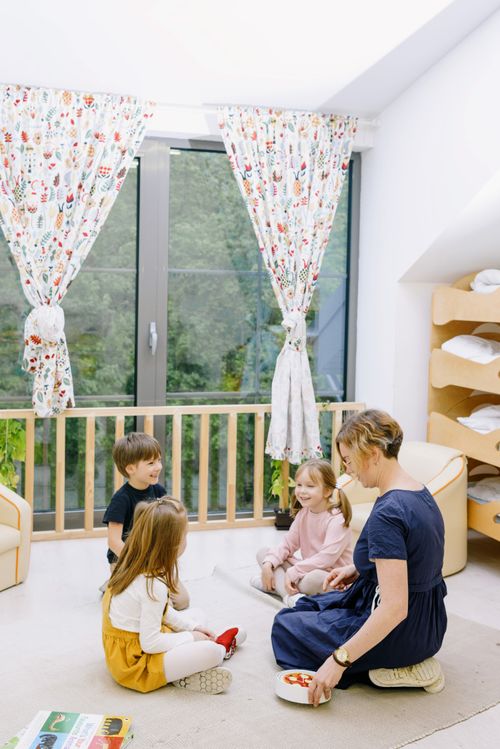 Free A mother playing and interacting with three young children in a bright, cheerful living room filled with natural light. Stock Photo