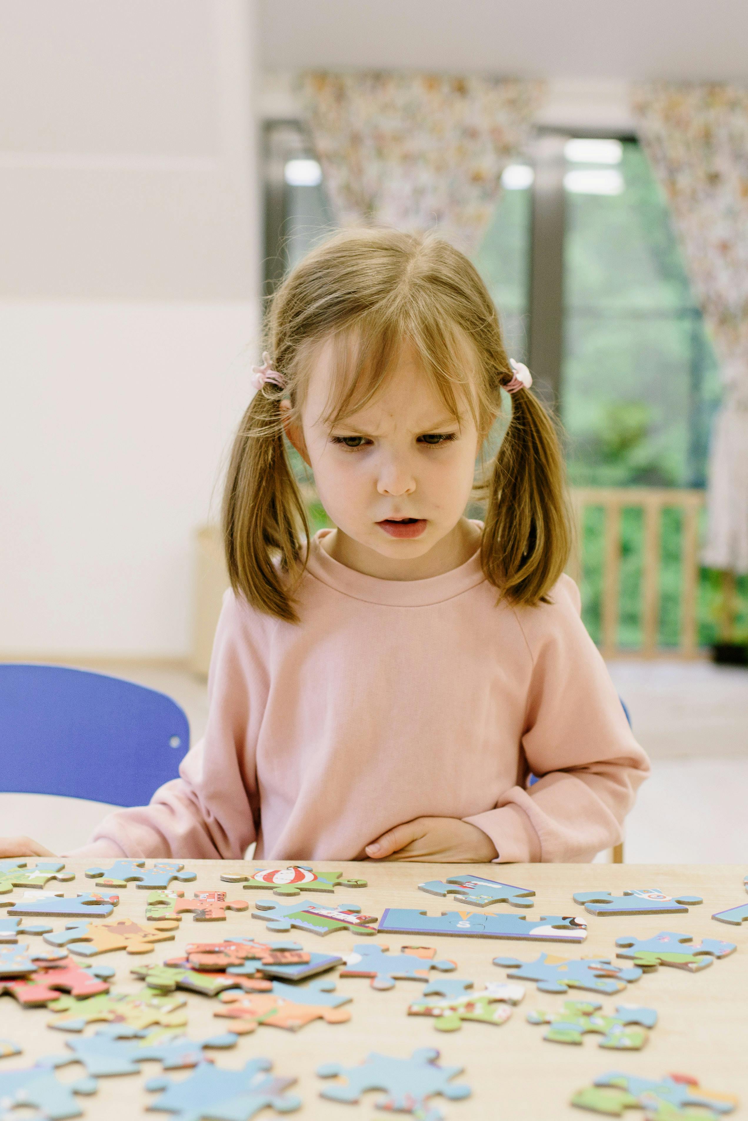 girl in pink sweater sitting looking at the puzzle pieces