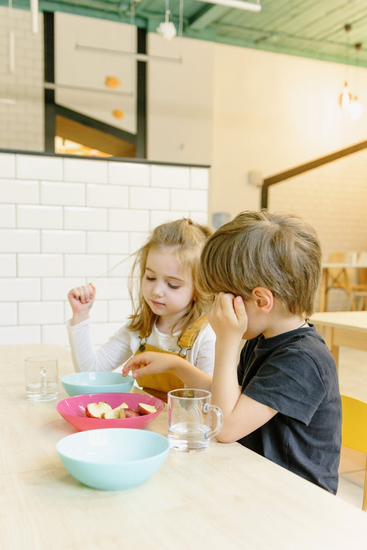 Boy And Girl Sitting Beside Each Other And Eating Apple Slices