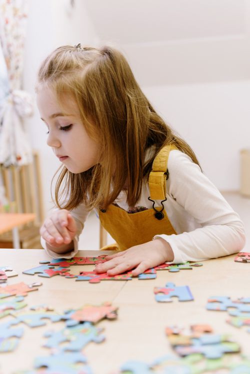 Free Young girl focused on assembling colorful puzzle pieces indoors, wearing yellow overalls. Stock Photo