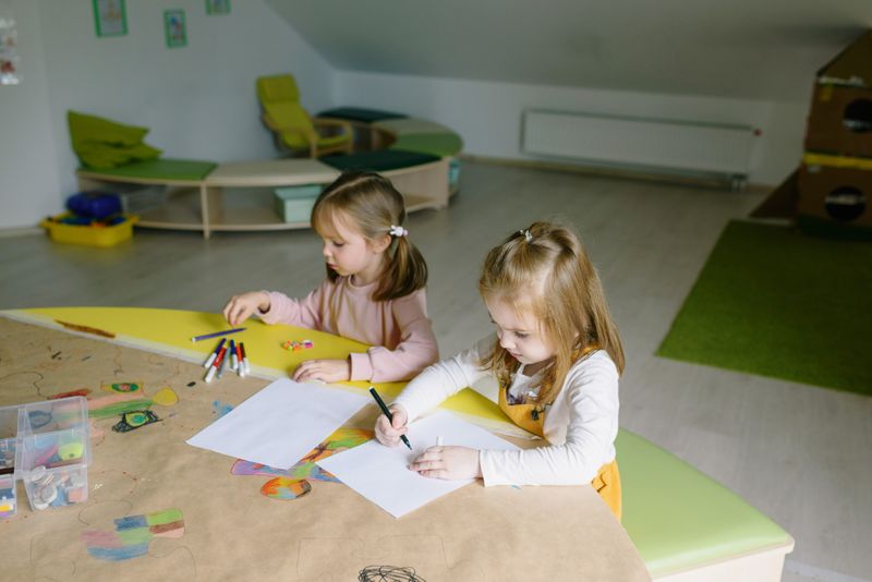 Dua anak menggambar menggunakan spidol warna dan kertas di kelas