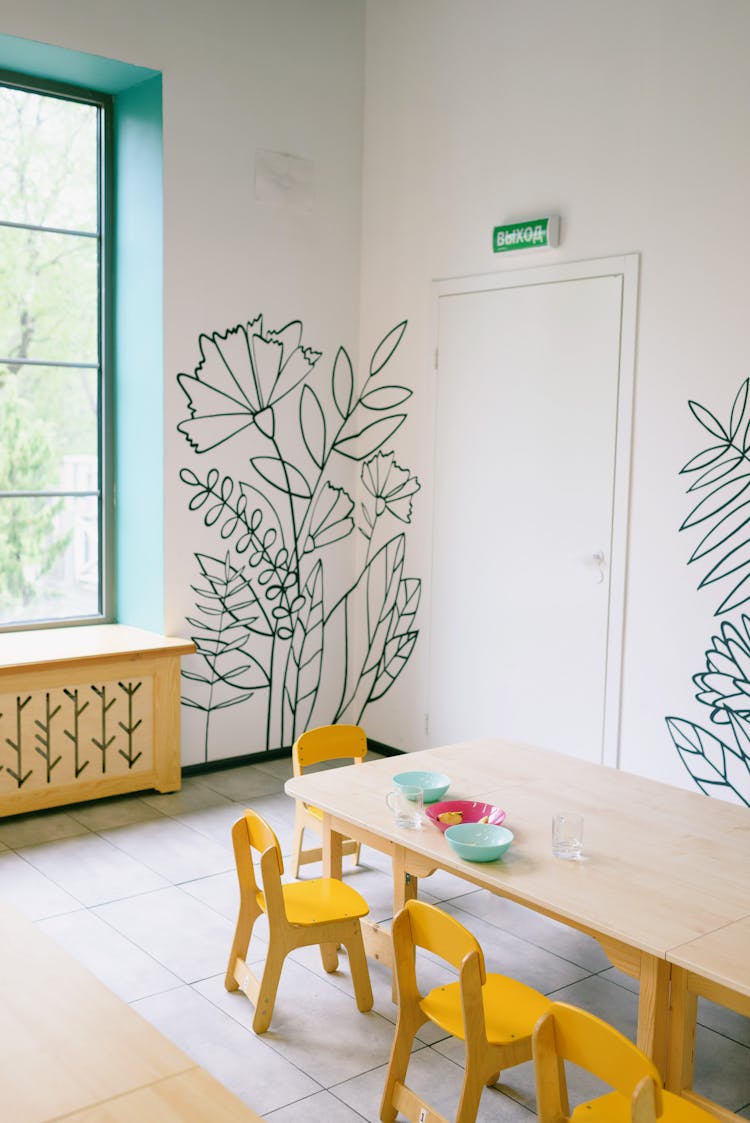 Room With Painted Flowers On Wall And Wooden Table With Yellow Chairs