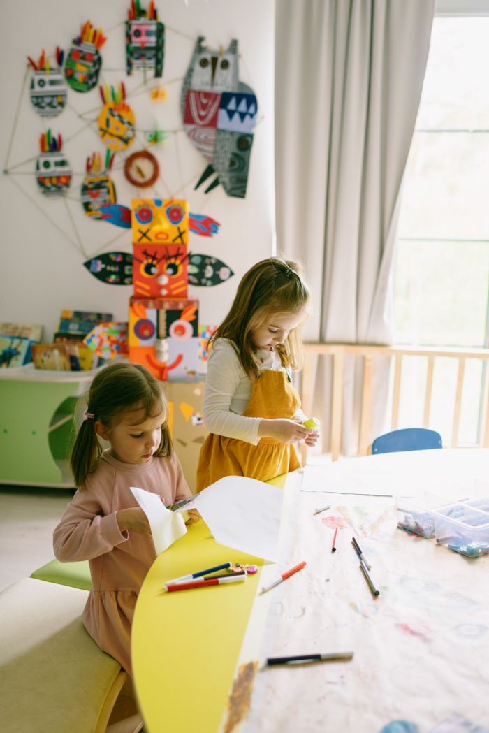 Two young girls cutting coloured paper in a workshop room
