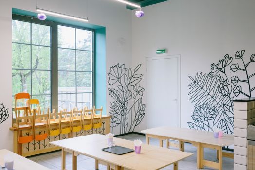 Empty kindergarten classroom with artistic floral wall designs and neatly arranged chairs and tables.