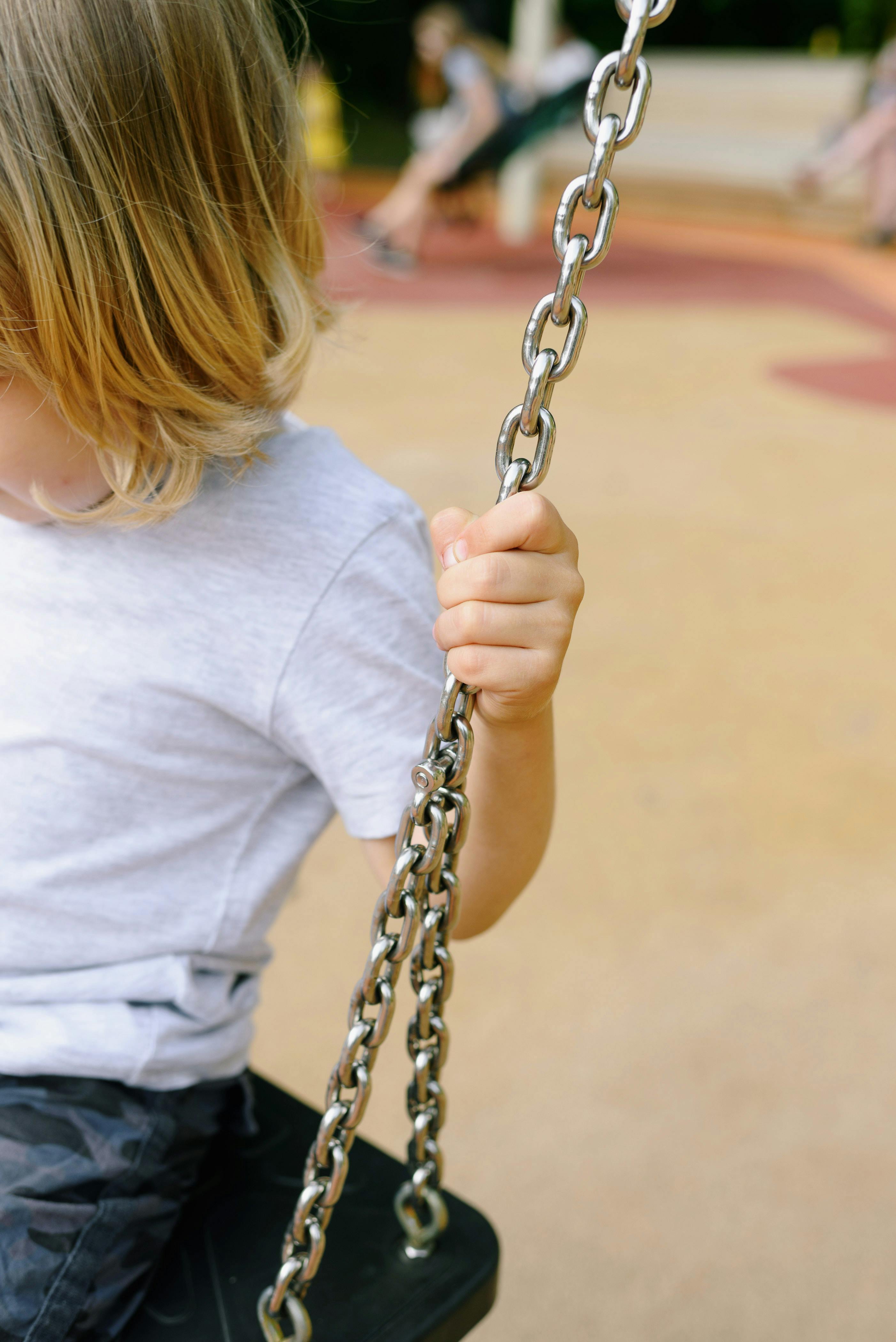 a kid sitting on a swing while holding on a metal chain