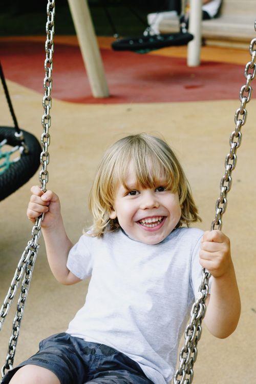 Free Happy child swinging on a playground swing outdoors on a bright day. Stock Photo