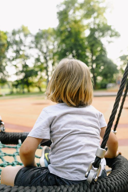 Free Rear view of a child with blonde hair sitting on a playground swing outdoors. Stock Photo