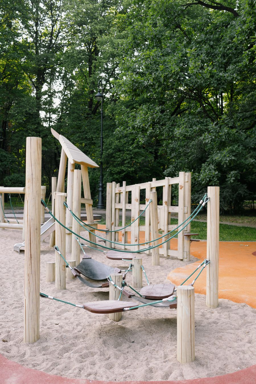 Medinė lauko žaidimų aikštelė su virvėmis ir smėliu tarp medžių