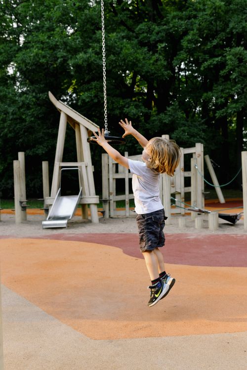 Free A young boy jumps joyfully at a playground swing on a sunny day, capturing fun and freedom. Stock Photo