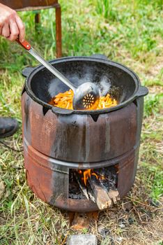 A rustic outdoor cooking scene with frying in a pot over an open fire using firewood.