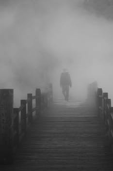A person walks on a misty wooden bridge surrounded by fog in Unzen, Japan.