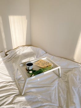 Minimalist scene of a breakfast tray with coffee, book, and tulips on a bed.