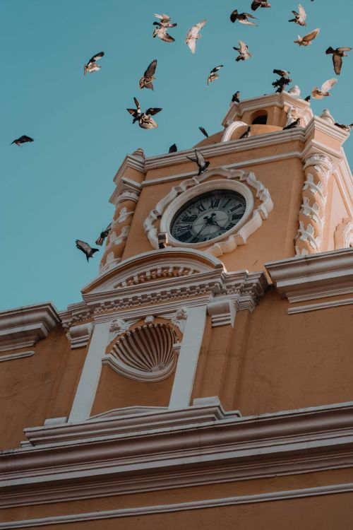Free A beautiful colonial clock tower with birds flying above, located in Antigua Guatemala. Stock Photo