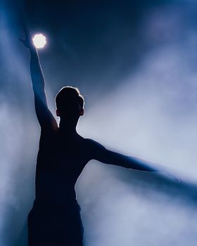 Silhouette of a dancer backlit by a bright light, surrounded by smoke, creating a dramatic scene.