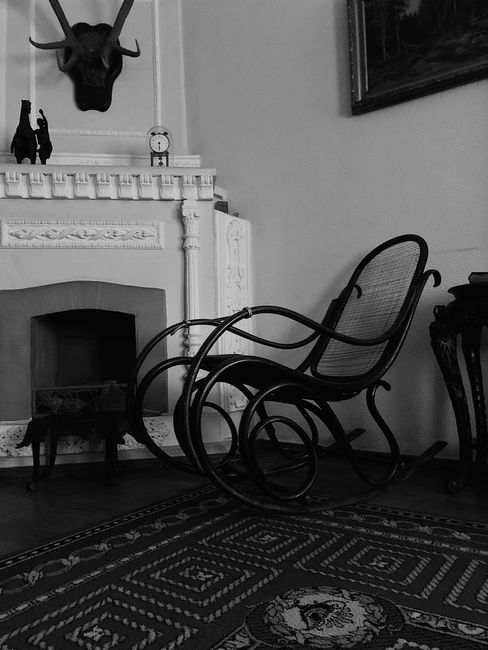 Black and white interior featuring a classic rocking chair, ornate fireplace, and vintage decor.