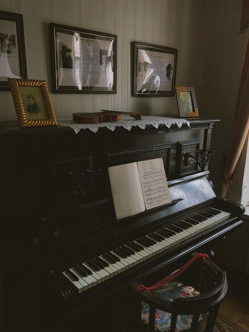 A vintage black upright piano with music sheets and framed photos in a cozy room.