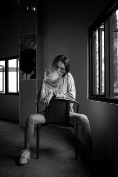 A fashionable woman smoking while sitting on a chair indoors, captured in monochrome.