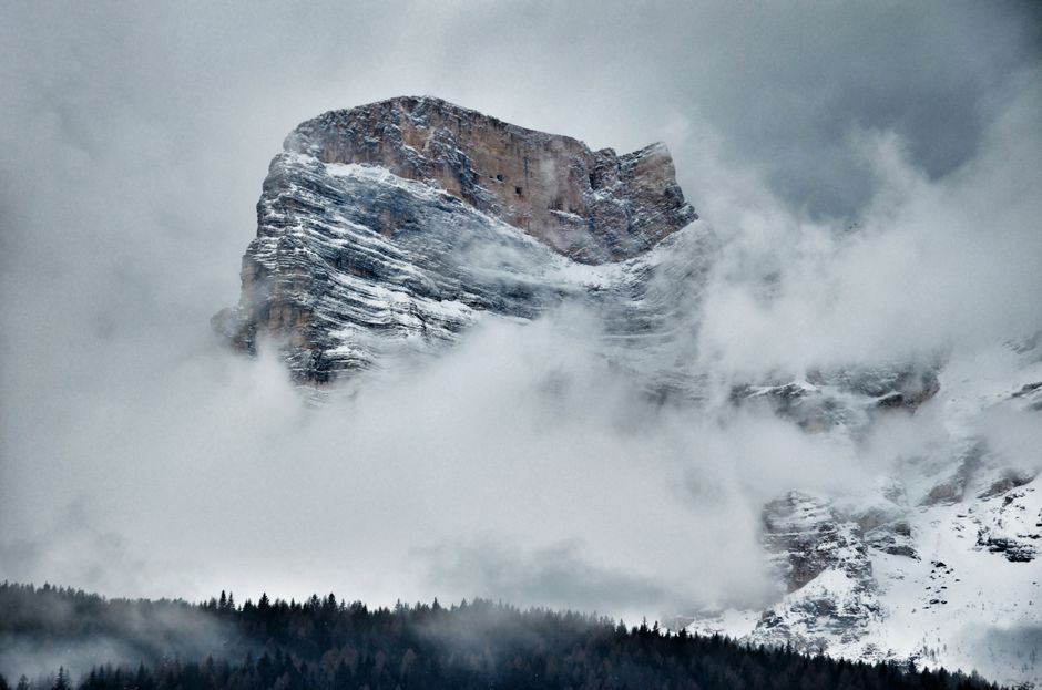 Majestic snow-covered mountain peak surrounded by dense fog in winter landscape.