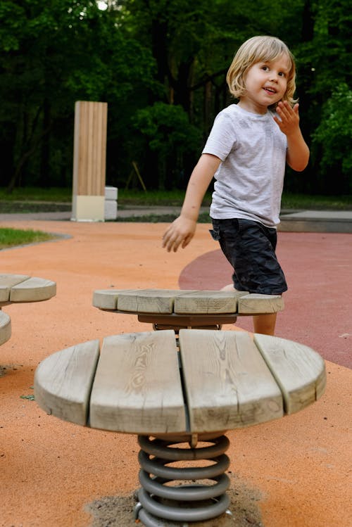 A Boy Playing on the Park Near Wooden Chairs