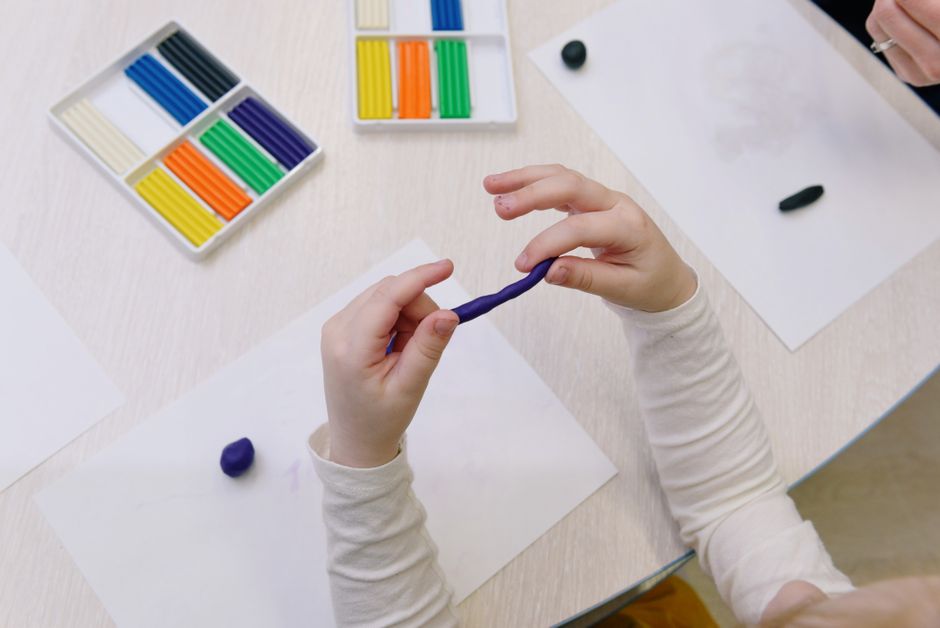 Overhead view of a child shaping purple modelling clay, surrounded by colorful clay sticks.