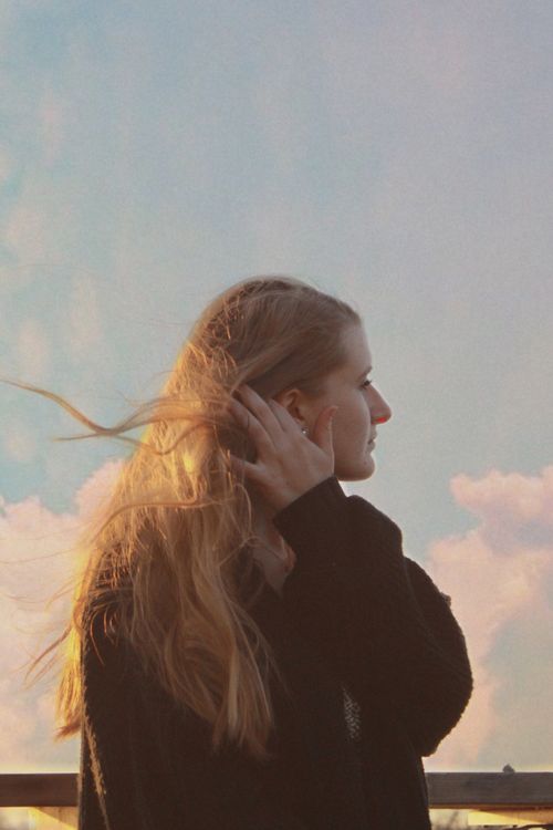 Free Woman in black sweater managing her messy hair against a serene sky backdrop. Stock Photo
