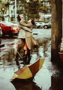 Couple hugging under rain with an umbrella down on a wet street, embracing love.