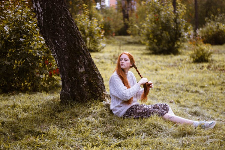 Woman Sitting On Green Grass Braiding Hair