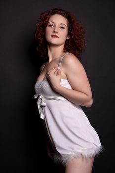 Portrait of a woman in white lingerie against a dark background, exuding elegance and confidence.