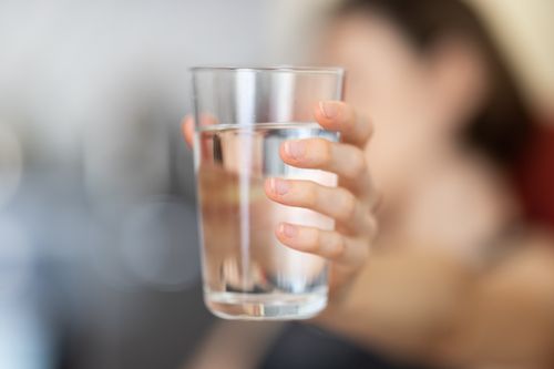 Free A hand holding a clear glass of water with a blurred background for health and hydration concept. Stock Photo