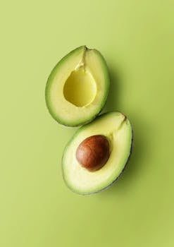 Close-up of fresh avocado halves on a vibrant green backdrop, showcasing its ripe texture.
