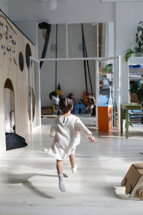Free A young girl joyfully runs through a bright, modern indoor playroom space. Stock Photo