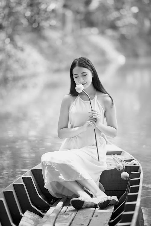 A Woman in White Dress Sitting in the Boat While Holding a Flower