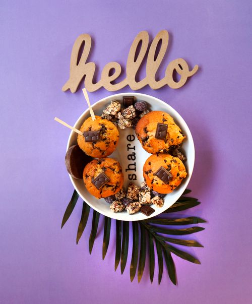 Free Close-up of homemade chocolate chip muffins in a bowl on a purple surface with decorative leaves and 'hello' text. Stock Photo