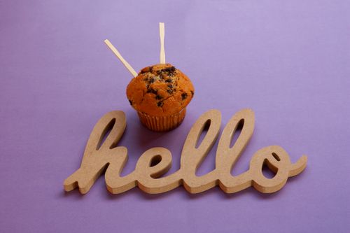 Free Close-up of a chocolate chip muffin and wooden hello sign on a purple background, perfect for greeting cards. Stock Photo