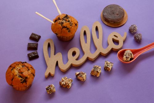 Free Creative arrangement of muffins and sweets with 'hello' on purple surface. Perfect for dessert enthusiasts. Stock Photo