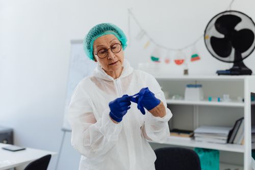 Free Elderly female scientist wearing PPE and gloves in a laboratory setting. Stock Photo