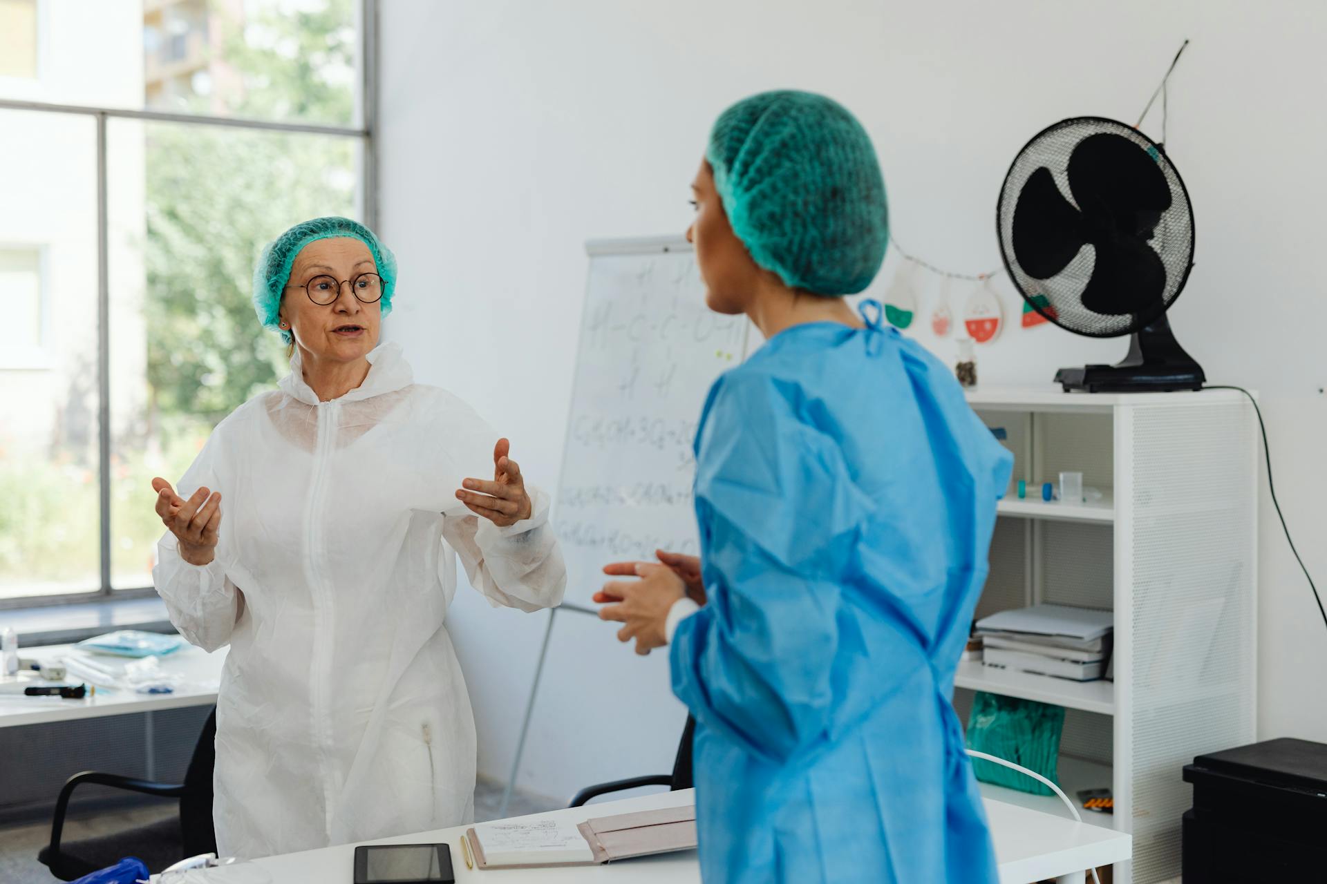 Two medical professionals in protective gear having a discussion in a clinic setting.