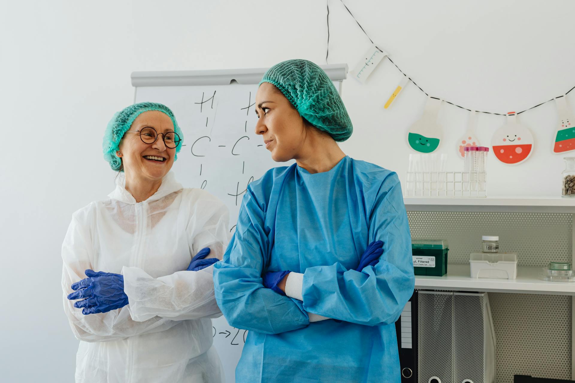 Two female healthcare workers in lab attire smiling and standing in a laboratory.