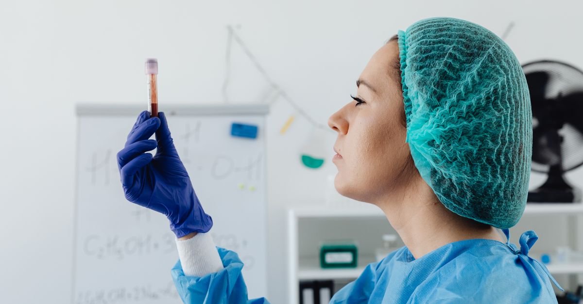 A laboratory scientist in protective gear inspecting a blood sample vial