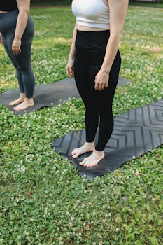 Two women practicing yoga outdoors on mats in a summer park setting.