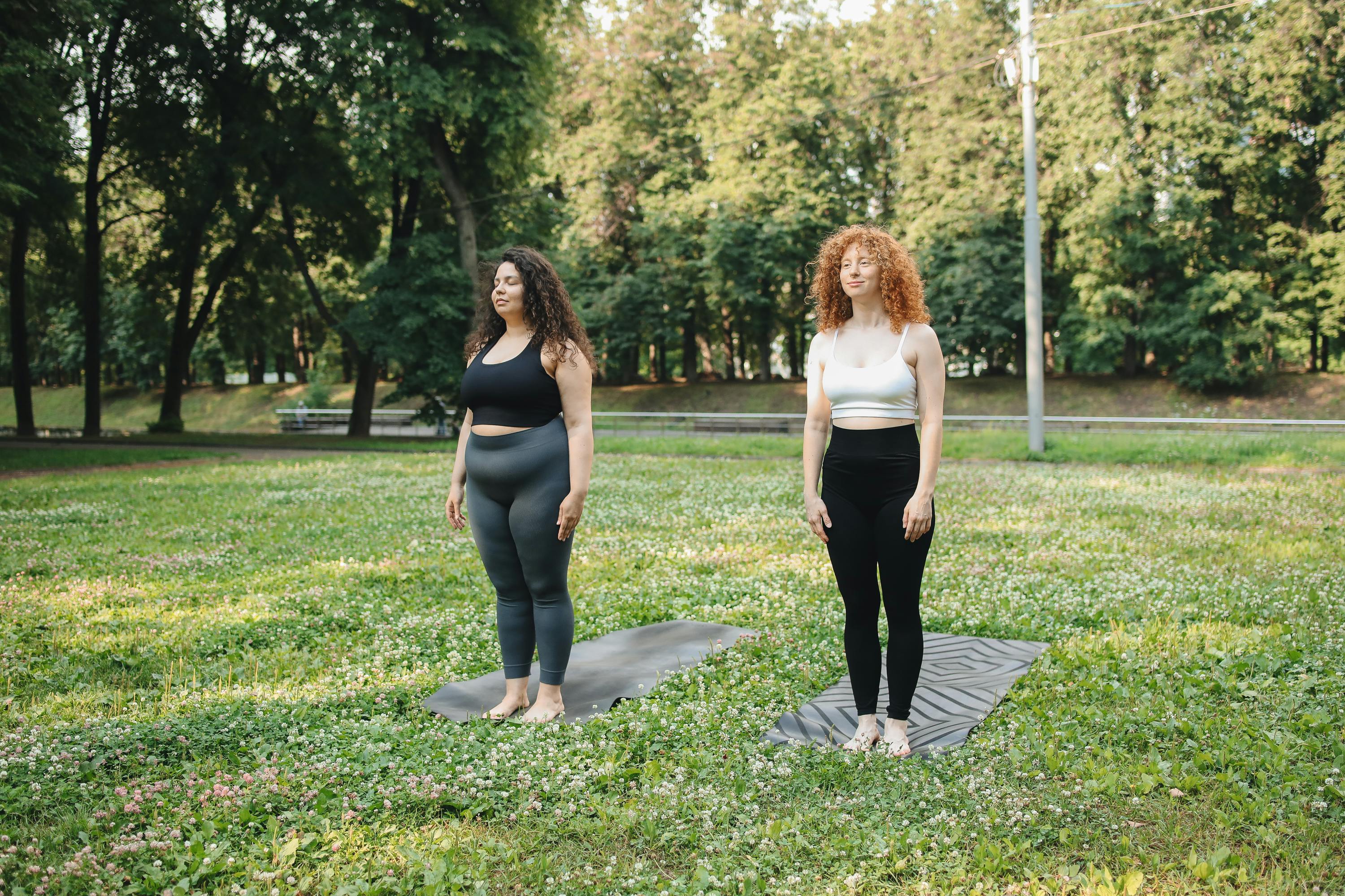 two women in leggings standing on yoga mat in the park