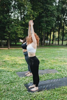 Two women practicing yoga outdoors in a serene park setting, focusing on wellness and flexibility.