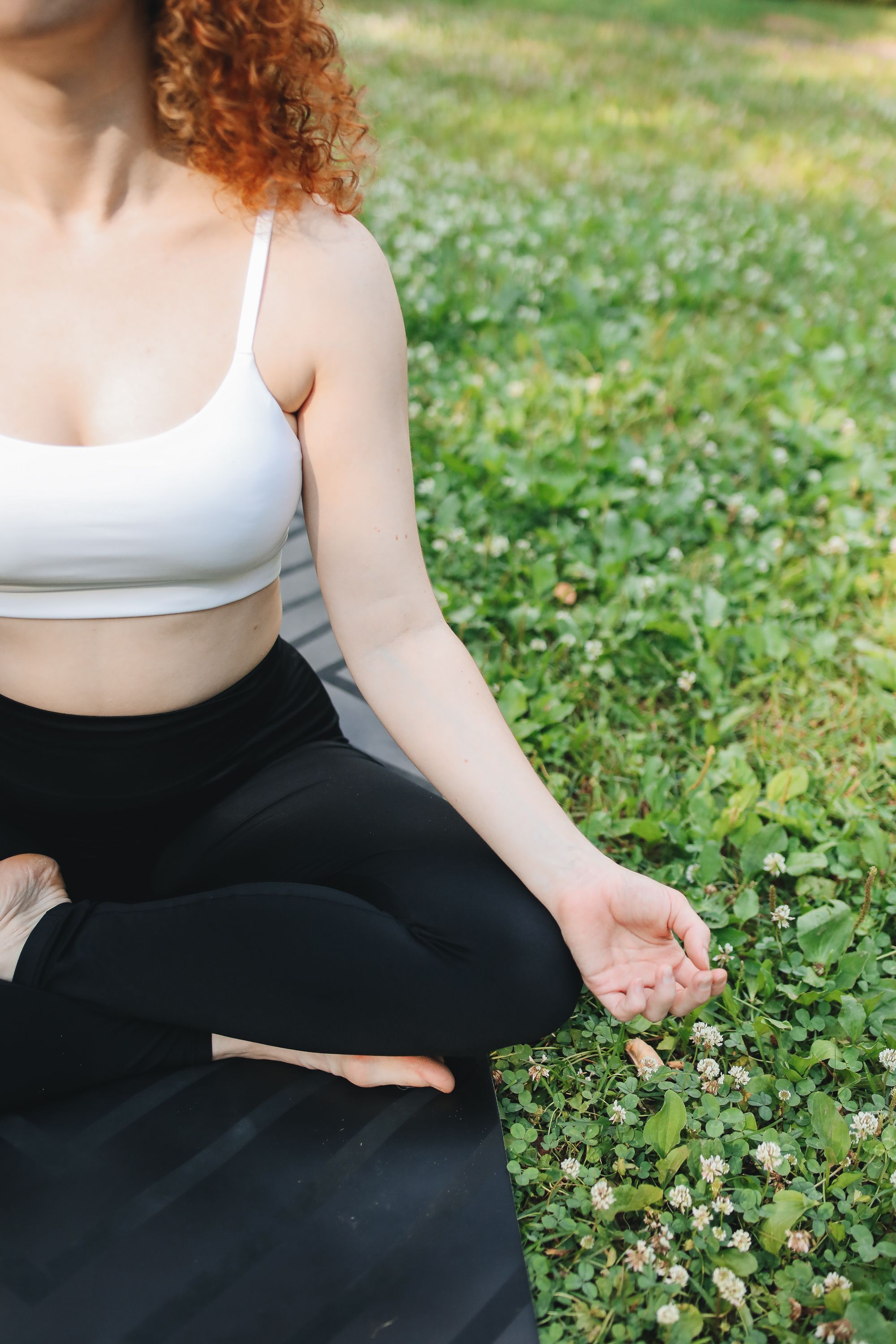 A person meditating outdoors on grass in activewear, promoting relaxation and well-being.
