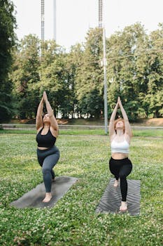 Two women engaging in yoga on mats in a sunny park, promoting healthy lifestyle and fitness.