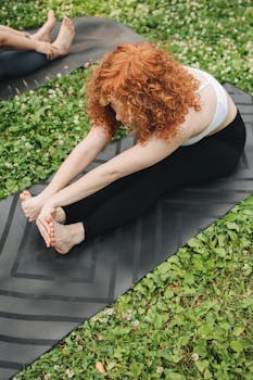 Redhead woman stretching on a yoga mat in a serene outdoor setting. Embrace wellness and relaxation.