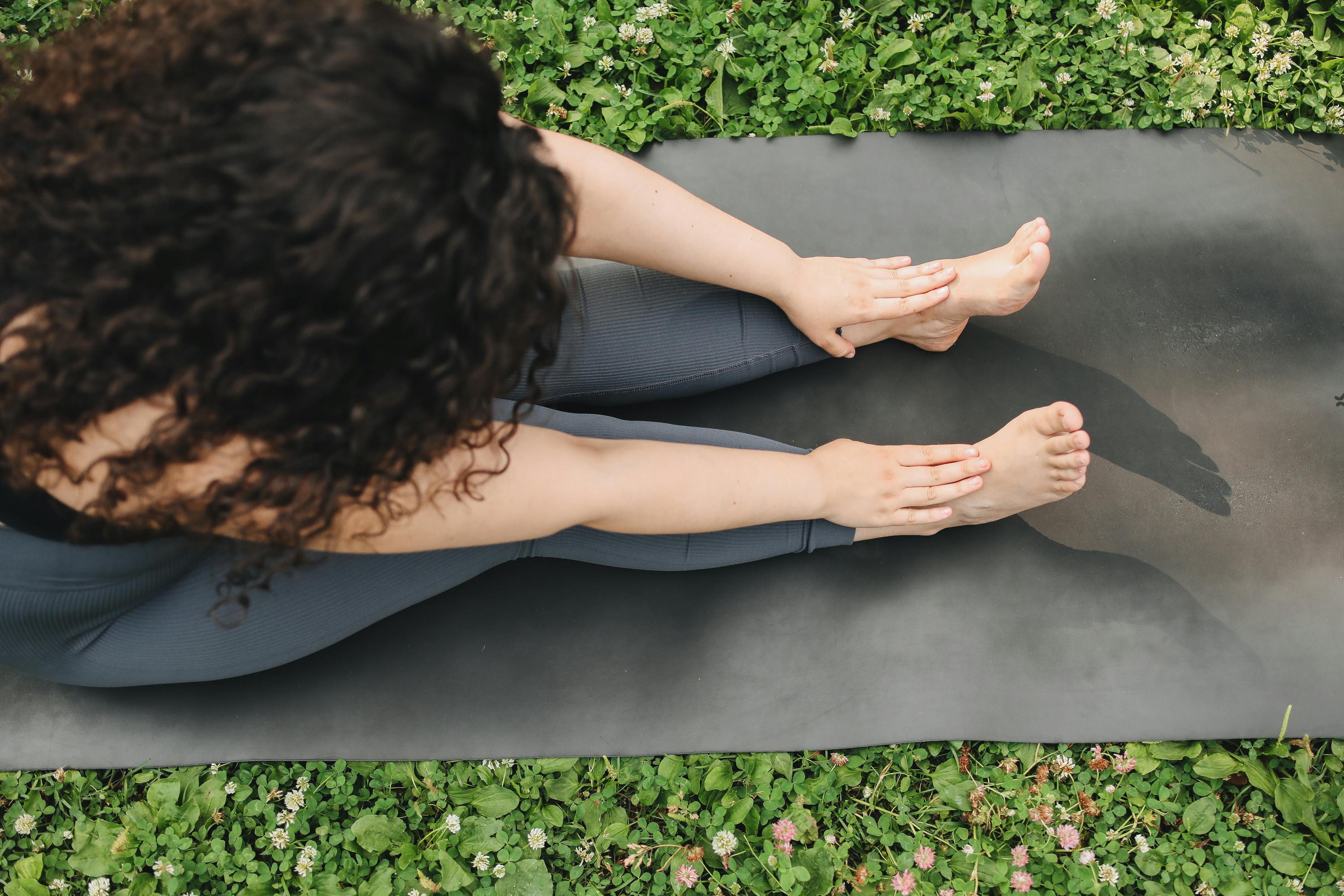 Aerial view of a woman stretching on a yoga mat in a grassy park setting.
