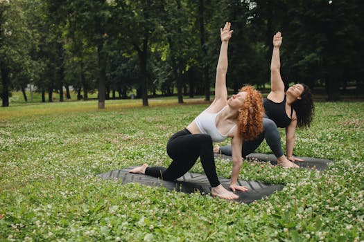 Two women practicing yoga poses on mats in a green park, focused on wellness and mindfulness.