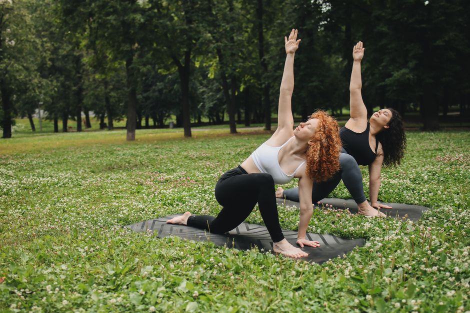 Two women practicing yoga together in a sunny park